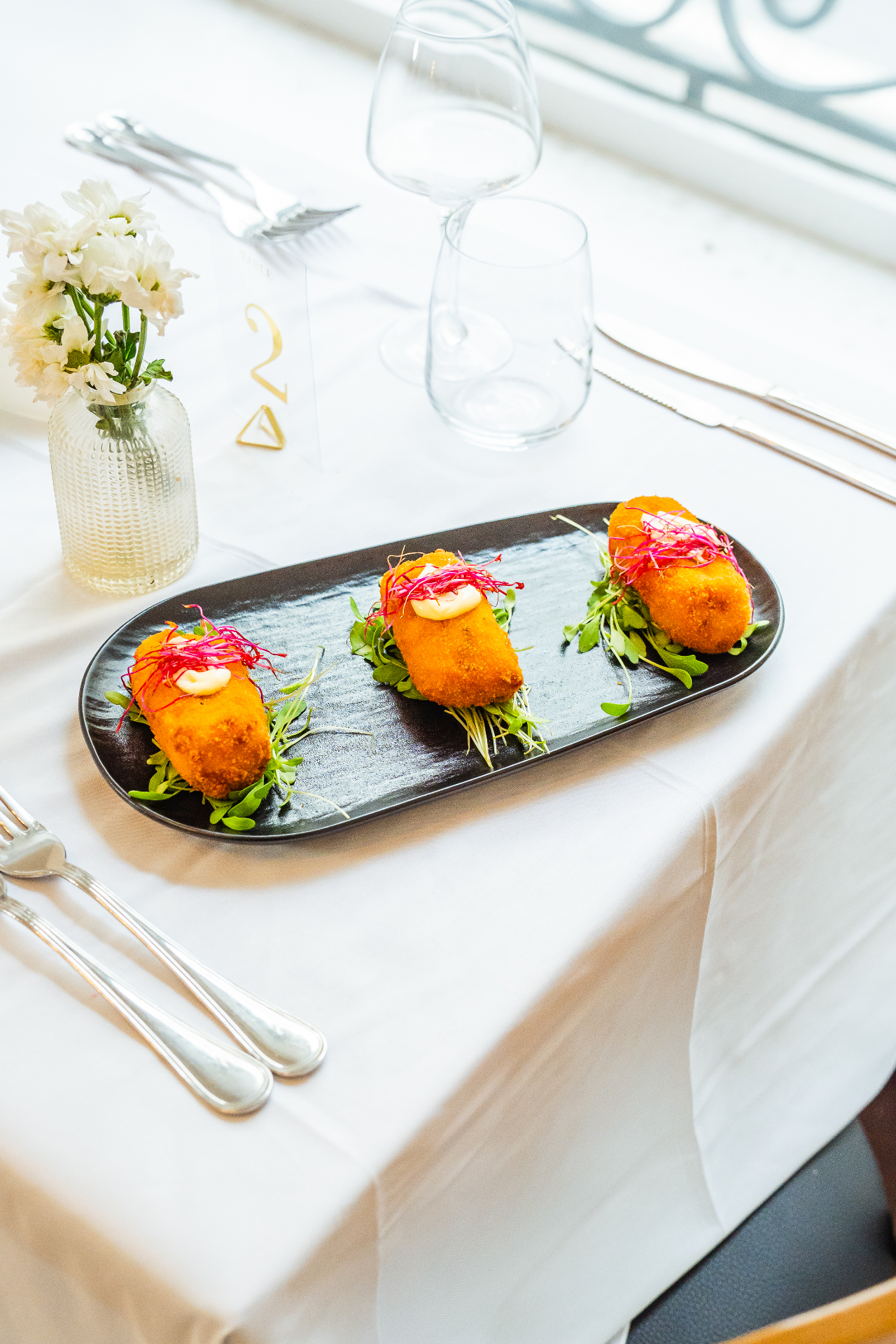 Trois croquettes de plantain dorées dressées sur ardoise noire avec émulsion mafé et pousses fraîches — entrée signature
