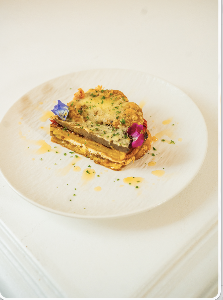 Part de lasagne au plantain gratinée au fromage, dressée à l'assiette avec fleurs comestibles — signature afro-européenne